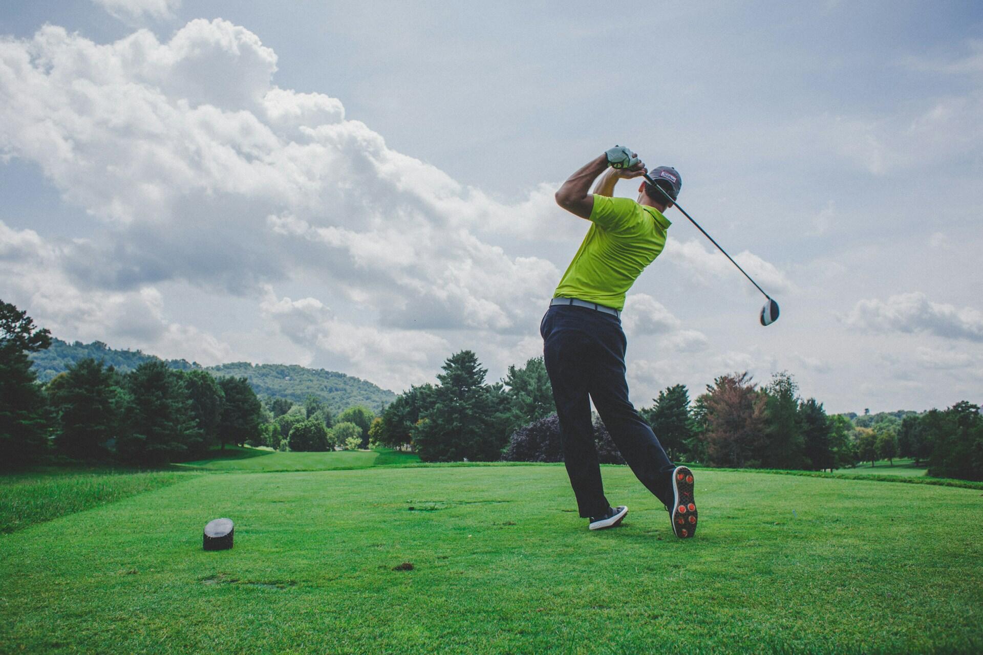 Un homme avec un club de golf frappe une balle sur un terrain de jeu. 